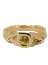 Load image into Gallery viewer, A yellow gold ring with a round natural diamond and hand-carved leaf detailing on a plain background.