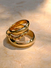 Load image into Gallery viewer, Two gold rings on a beige stone surface
